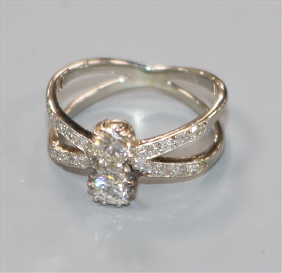 A white metal and two stone diamond set split shank ring, with diamond set shoulders, size K.